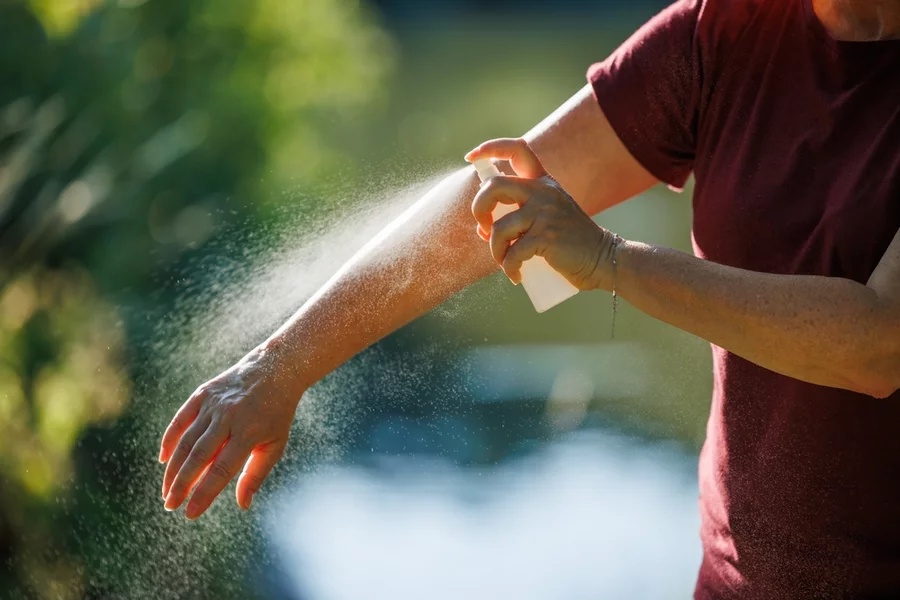 A woman spraying her arm with mosquito repellent.